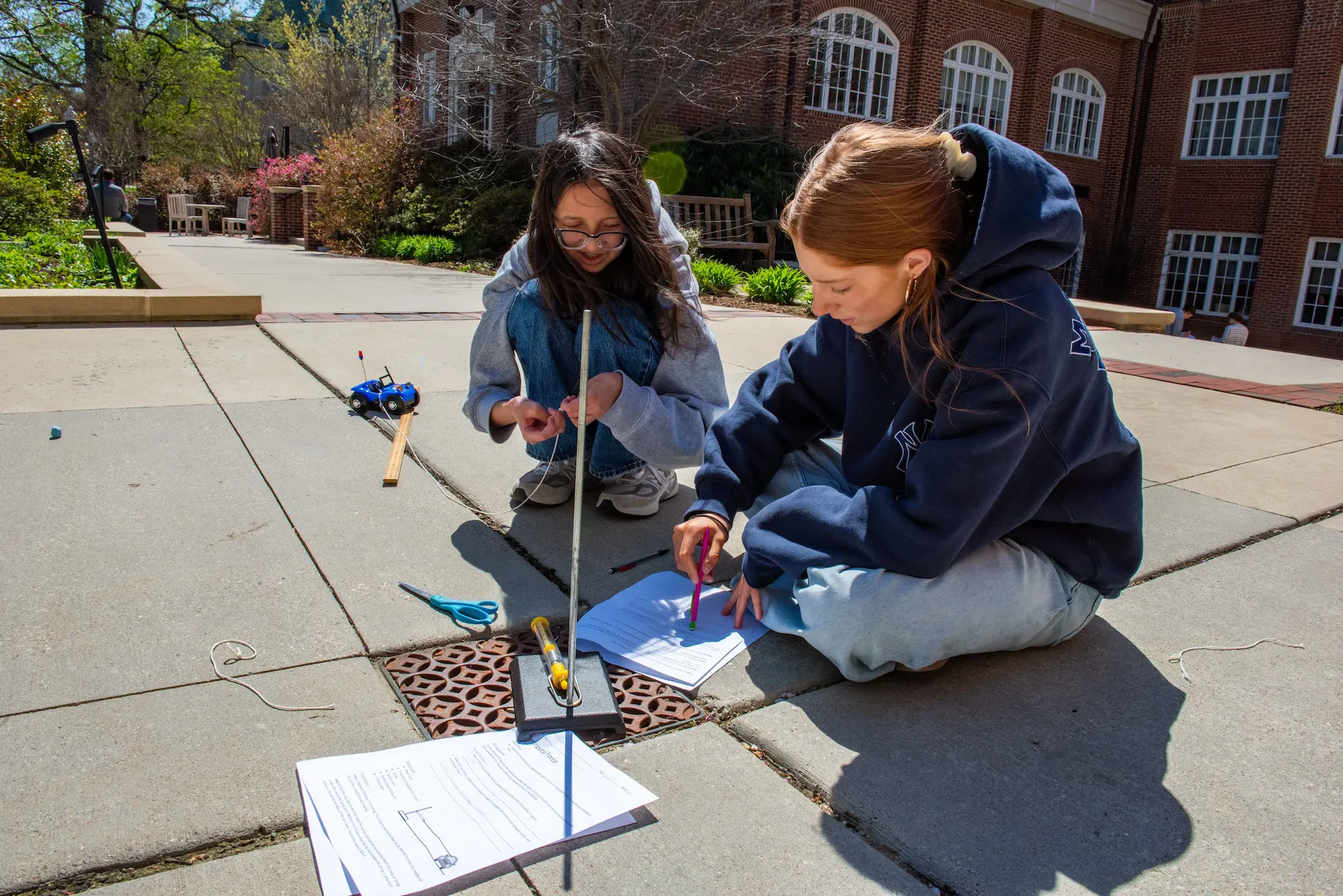 Two girls at NCS sitting on the floor outside working on something
